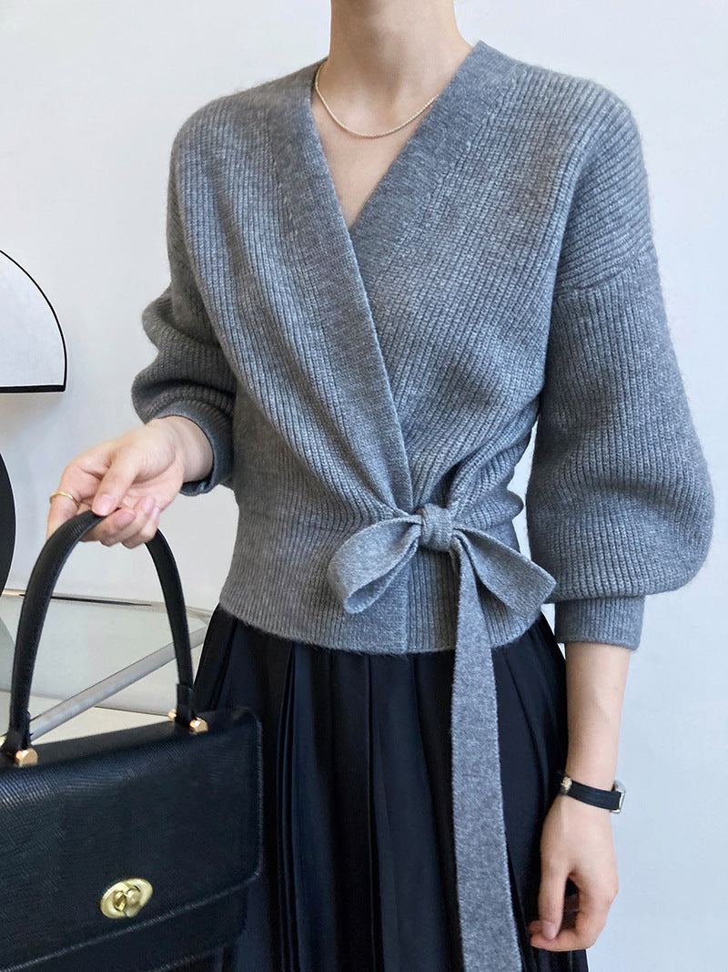 Gilet cache-cœur gris chiné en maille côtelée, manches bouffantes, porté avec une jupe plissée noire