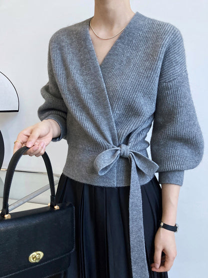 Gilet cache-cœur gris chiné en maille côtelée, manches bouffantes, porté avec une jupe plissée noire